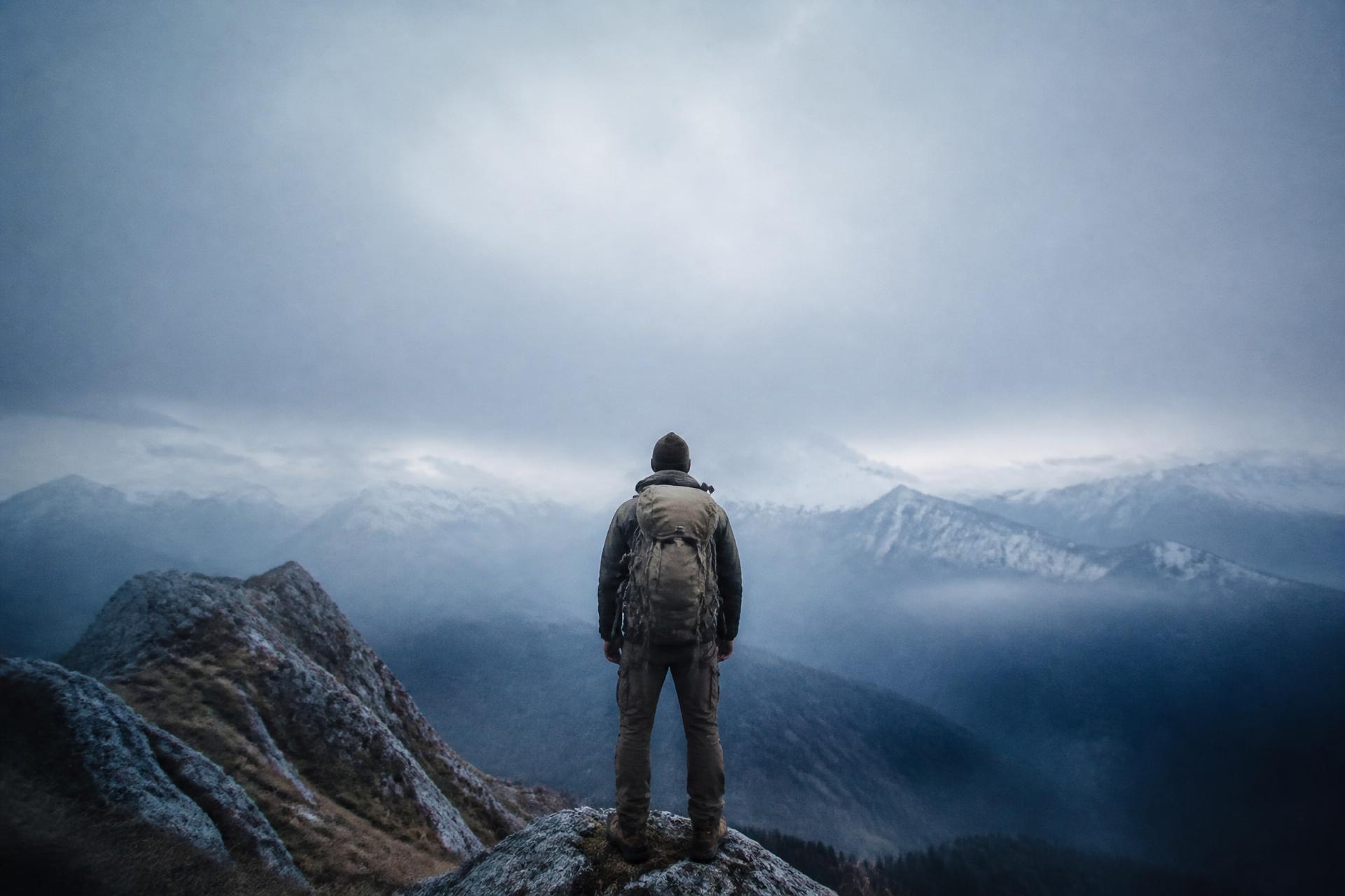 A lone traveller with a heavy pack at the edge of a misty mountain ridge at cold dawn