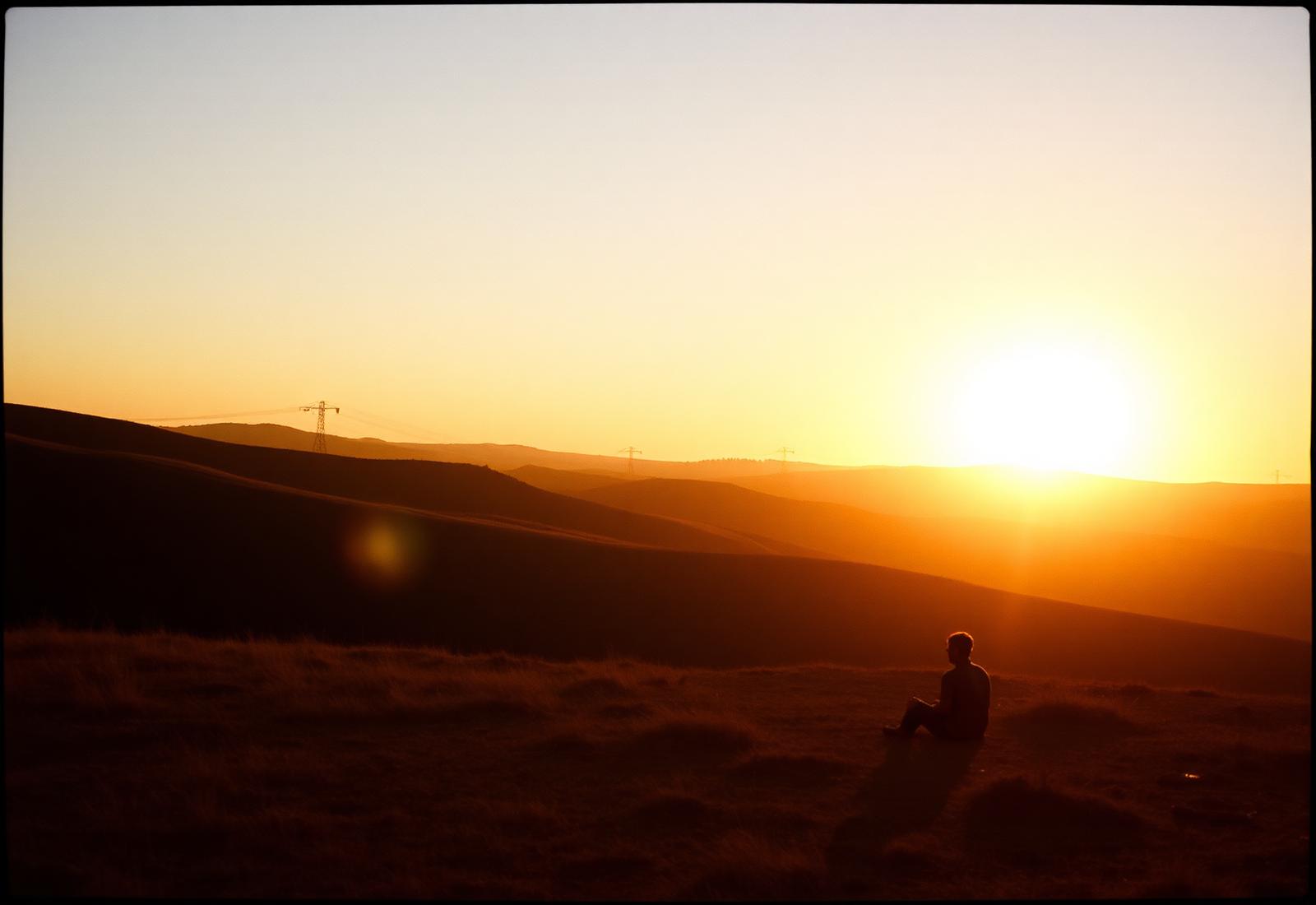 A single person watching a quiet golden sunrise over rolling hills